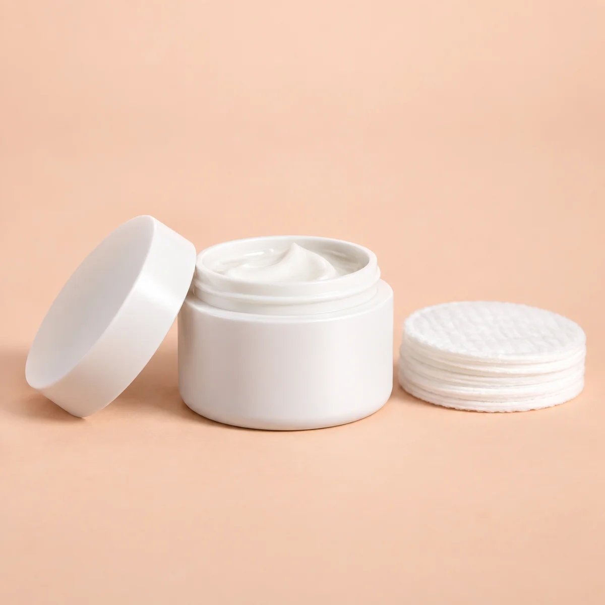 White cream jar and cotton pads on a soft peach background